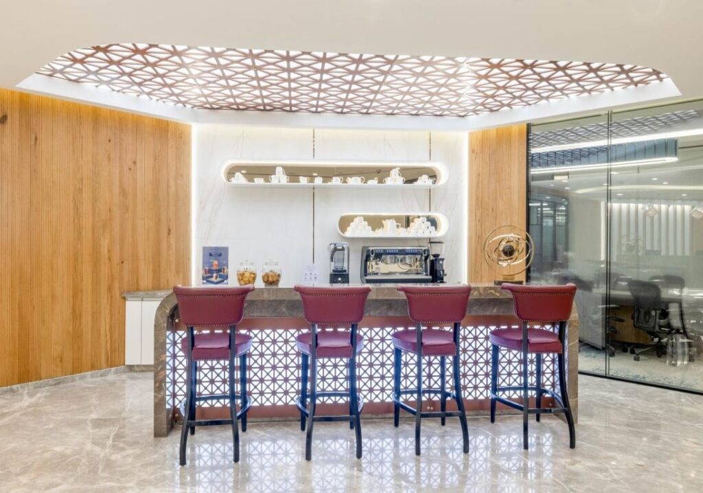 Members' bar: white marble counter with sculpted display niches, red velvet barstools, decorative lattice ceiling, glass-walled office visible through back wall.