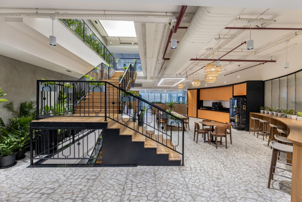 Internal stair with timber treads and black steel balustrades, hanging woven pendants, polished terrazzo floor with tile inlay, café seating alongside.