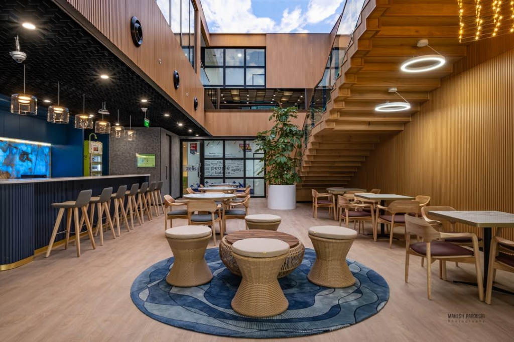 . Indoor-outdoor terrace: woven rattan stools at a long counter, copper-pipe pergola with hanging planters, biophilic edges, full-height glazing.